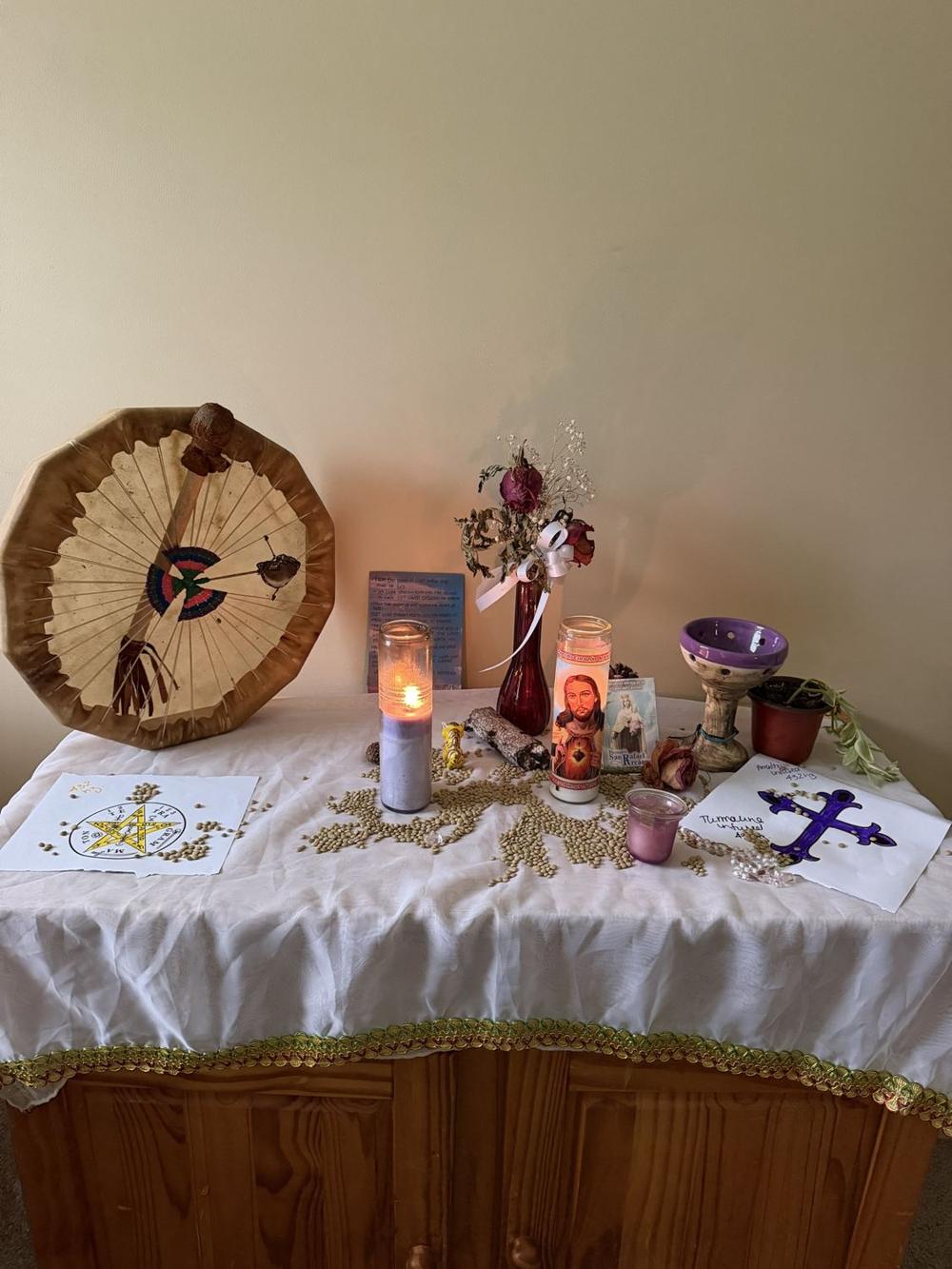Paola Andrea's home altar with a hand drum, candles, dried roses and sacred images.