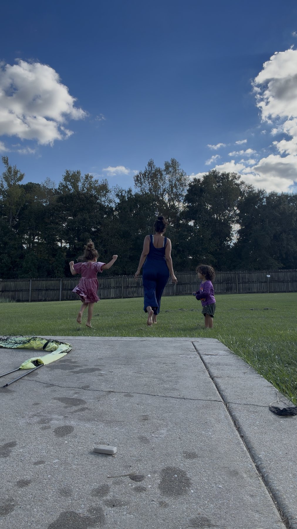 Paola Andrea and her two daughters walking barefoot across the grass under a blue sky.