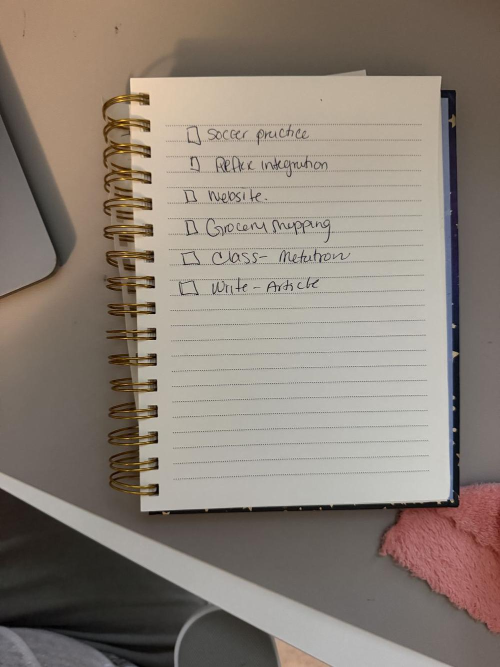 A handwritten to-do list in a spiral notebook: soccer practice, website, grocery shopping, write article.